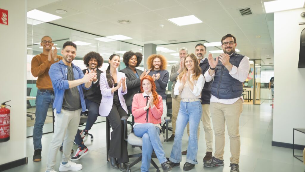 Office Professionals welcoming Temporary worker. Group of diverse office employees clapping and smiling in a modern office. They stand together, showing a positive and collaborative work environment.