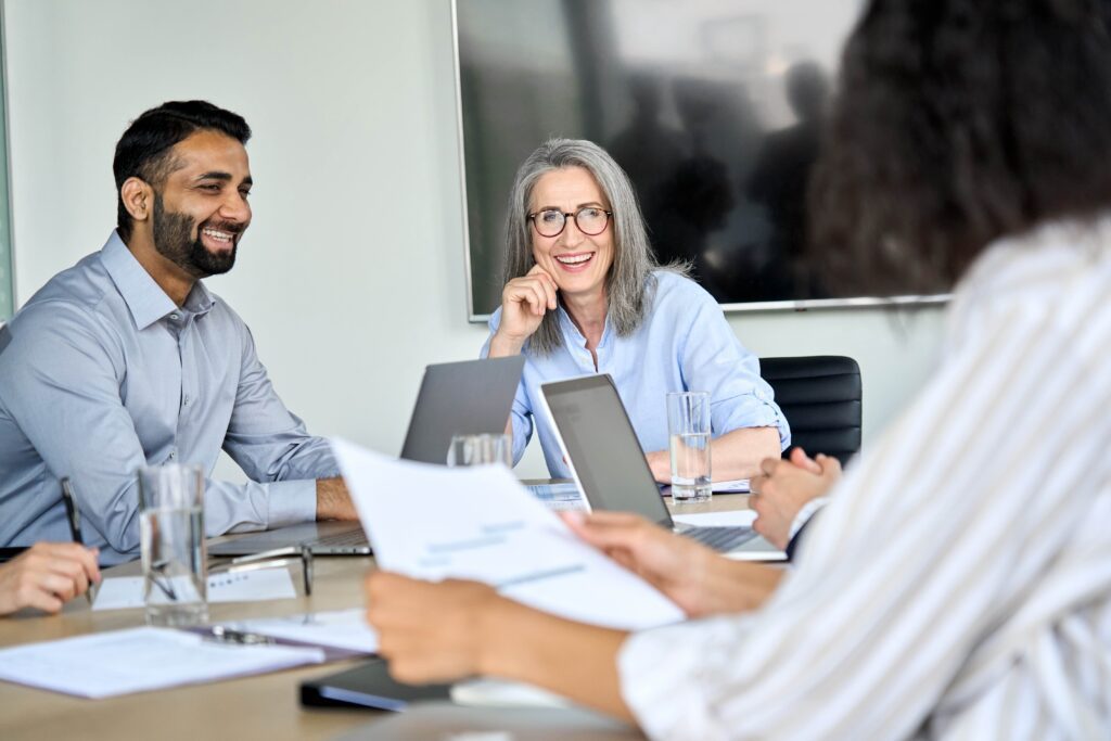 Employer smiling and enjoying the benefits of Temporary workers creating a more diverse team. Smiling diverse corporate team working together in modern meeting room office.