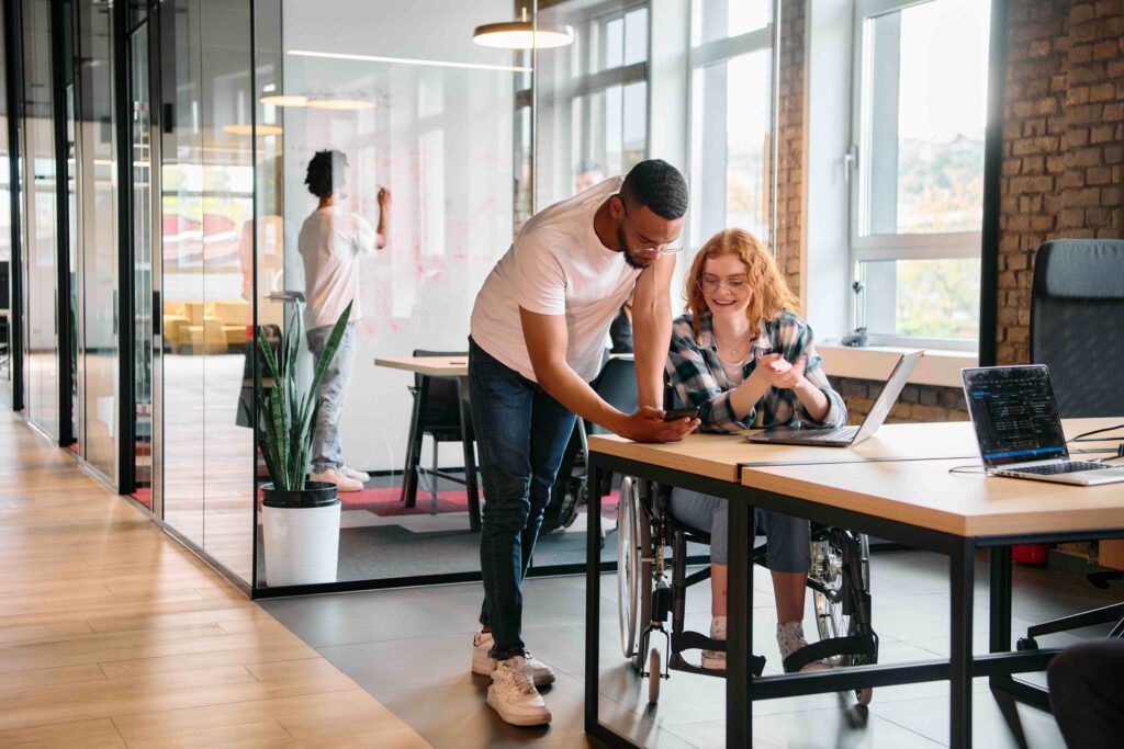 Inclusive Workplace, reasonable adjustments made in the workplace, Young man engages with Colleague who has is in a wheelchair.