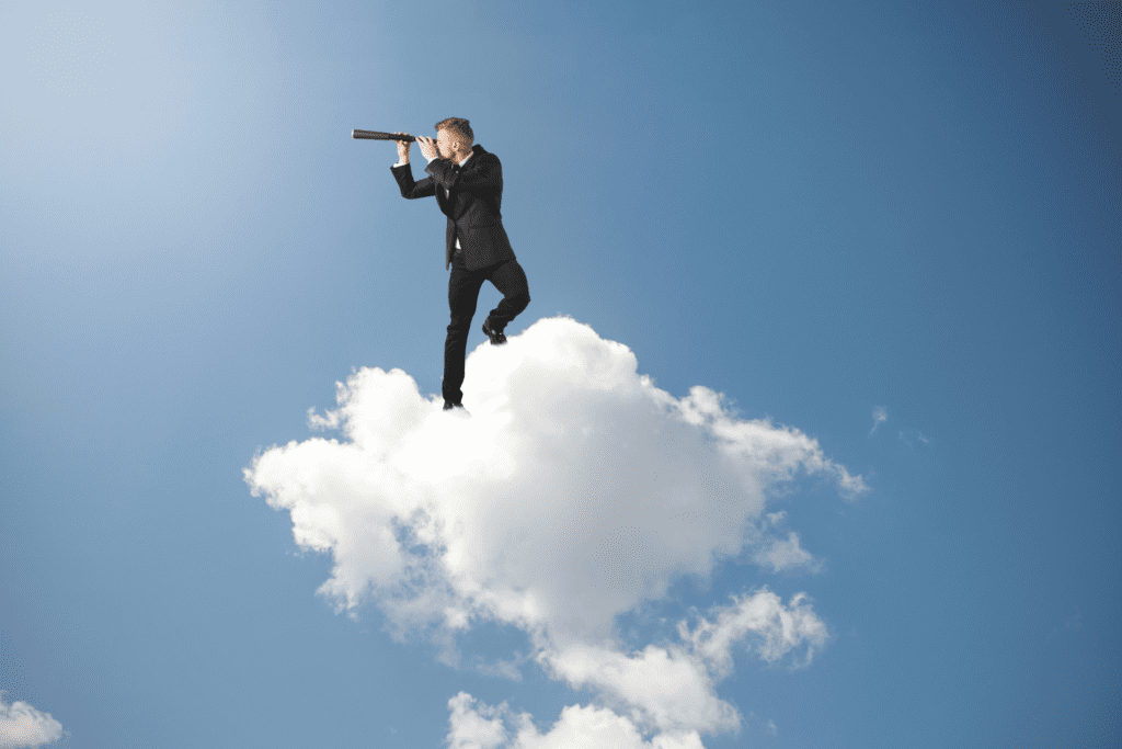 A businessman in a suit standing on a cloud, looking through a telescope, symbolising forward-thinking recruitment trends and hiring predictions for 2025.