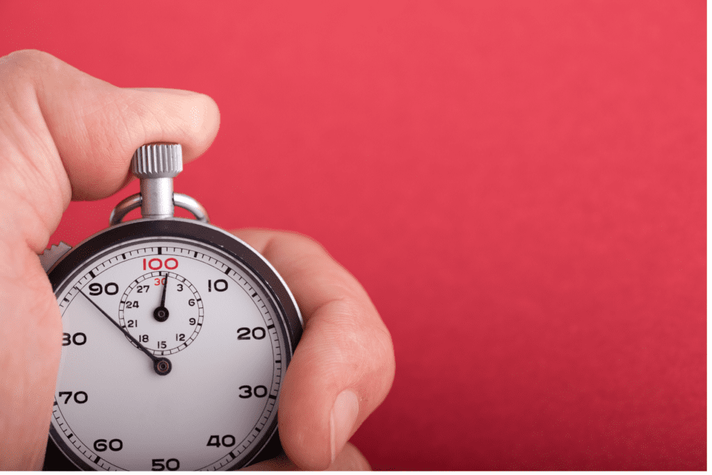 A hand holding a stopwatch against a red background, symbolising the importance of speed and efficiency in recruitment processes for 2025