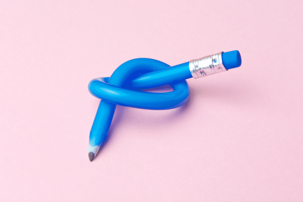 A flexible blue pencil tied in a knot on a pink background, symbolising adaptability and flexibility in recruitment trends for 2025.